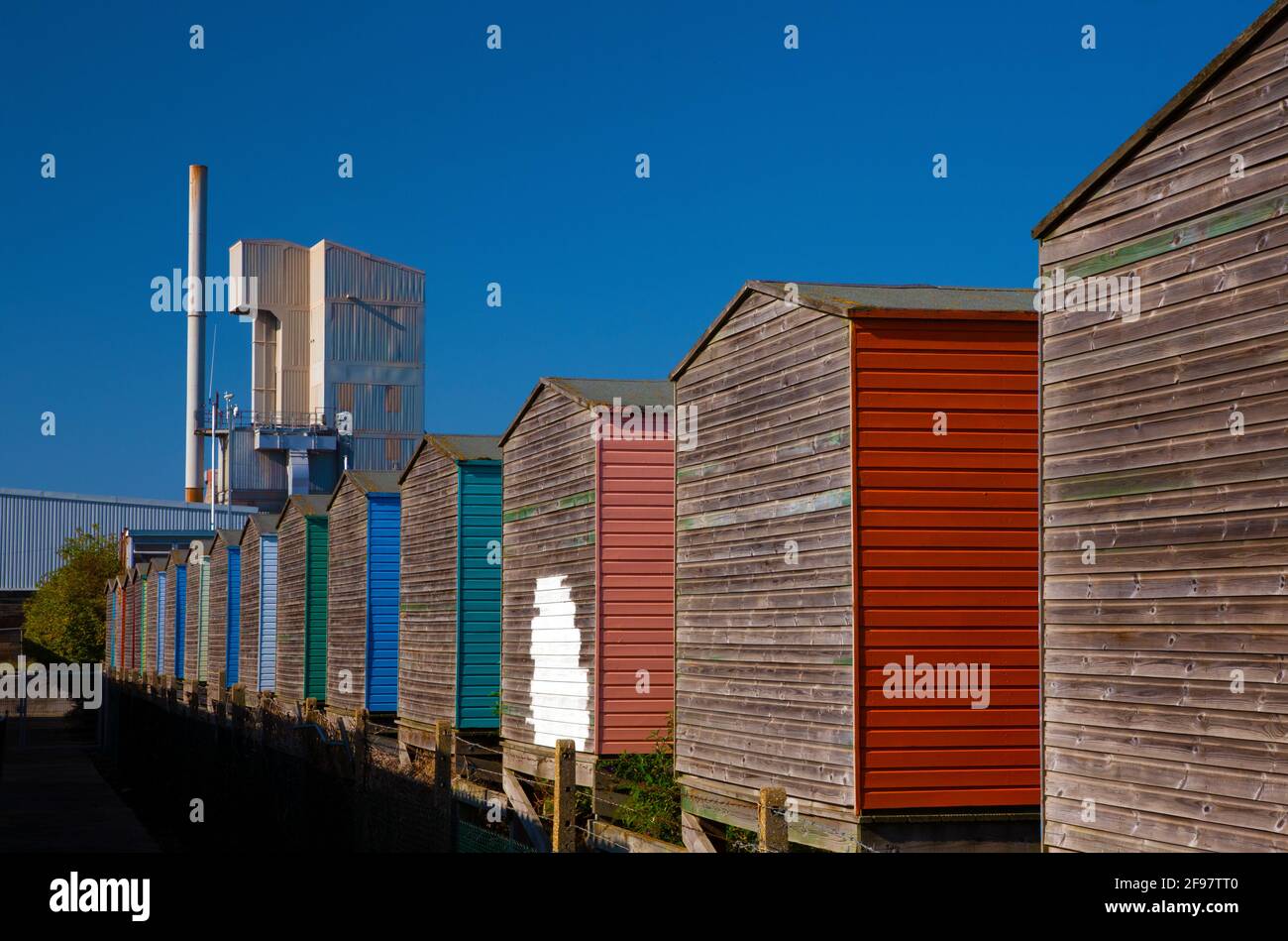 The Brett Aggregates factory overshadows traditional beach huts at Whitstable, Kent, UK. Stock Photo