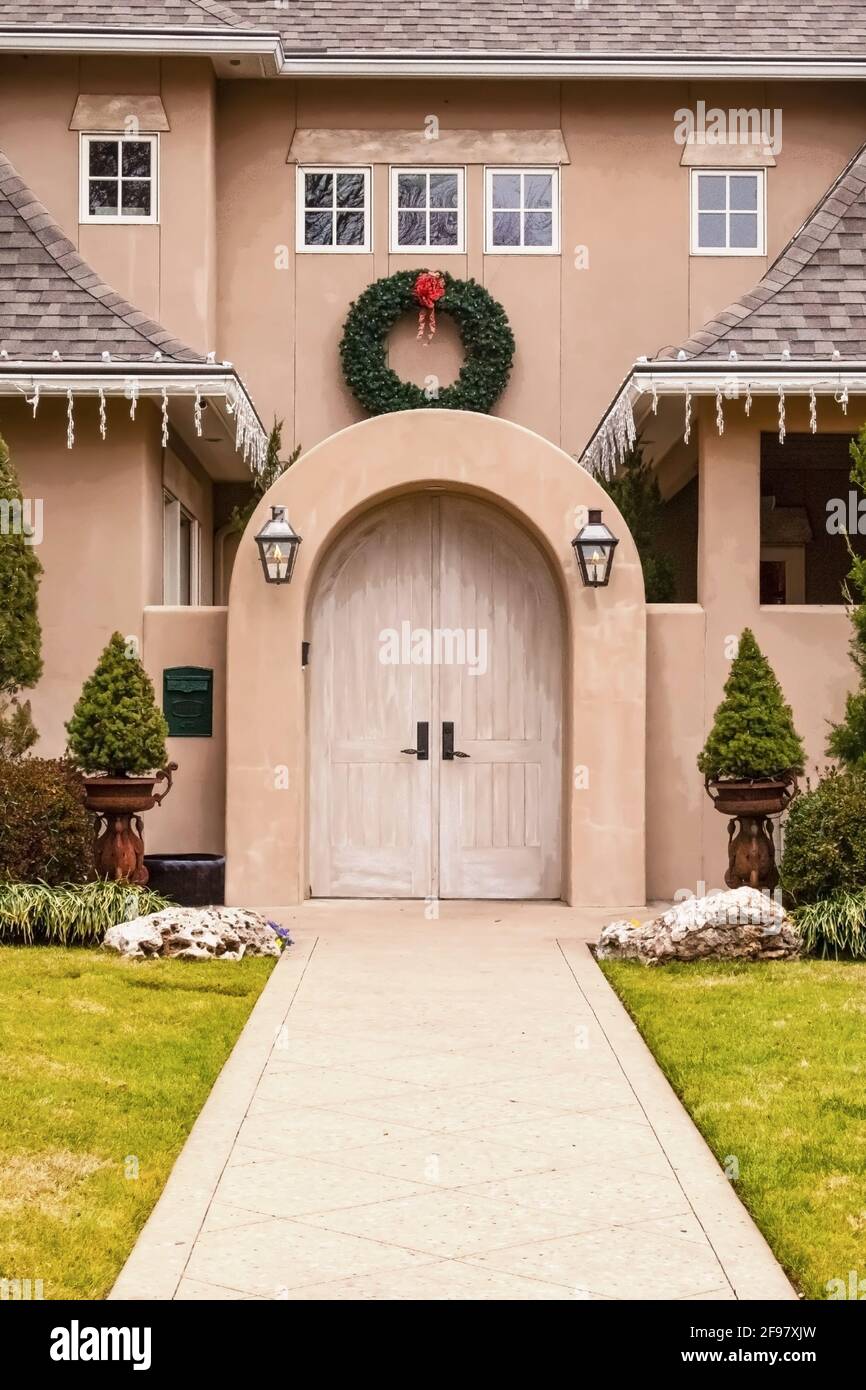 Arched entrance to upscale stucco house with Christmas wreath and lights and landscaping and sidewalk Stock Photo