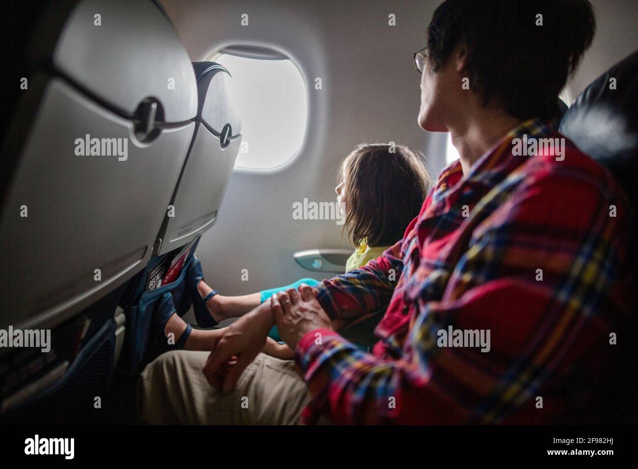 A little girl and father sit together on airplane looking out window Stock Photo
