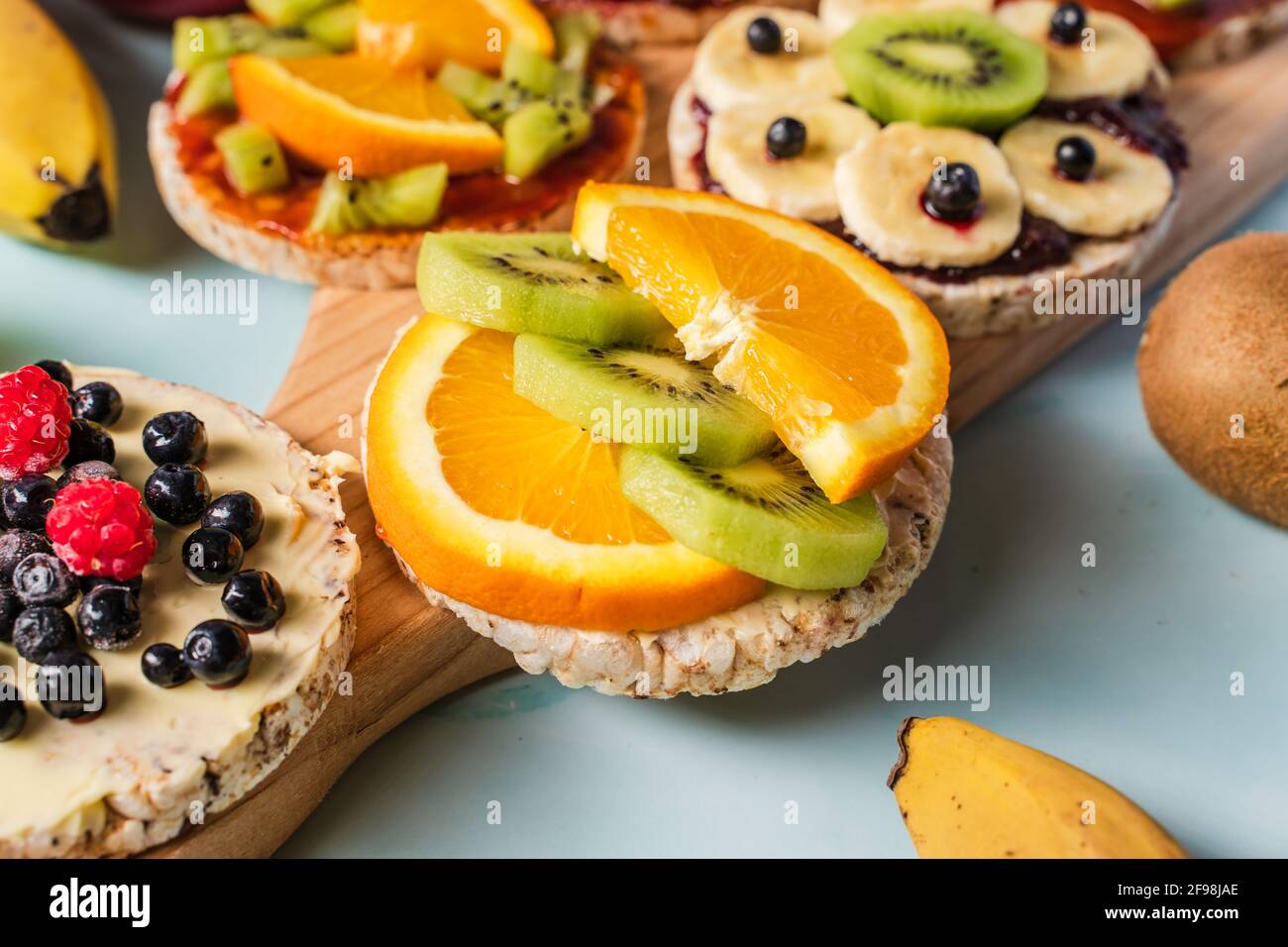 Crispy puffed rice cakes on table with fresh fruit kiwi banana apple blueberries and orange on the table - close up view on healthy organic vegetarian Stock Photo