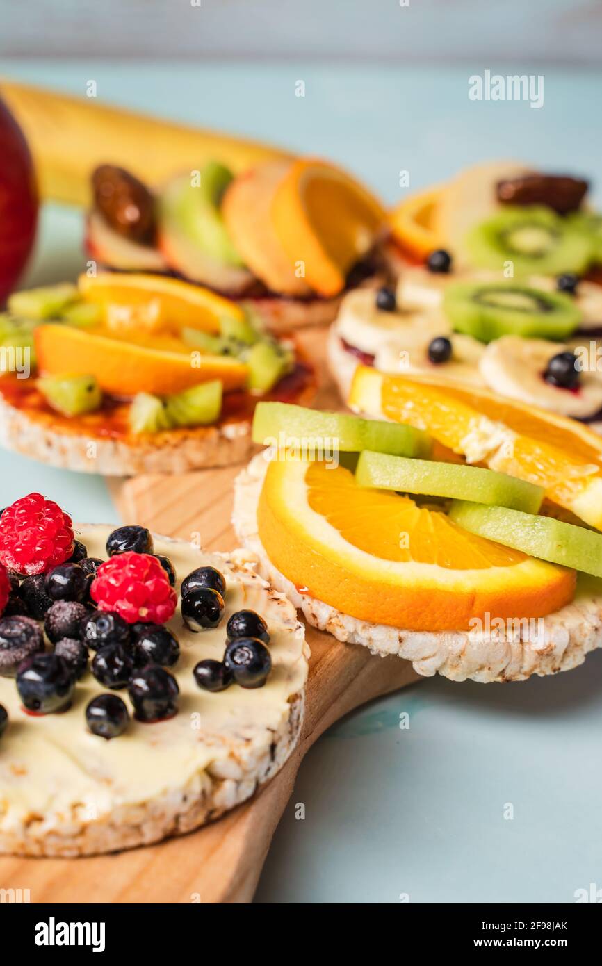 Crispy puffed rice cakes on table with fresh fruit kiwi banana apple blueberries raspberries and orange on the table - close up view on healthy organi Stock Photo