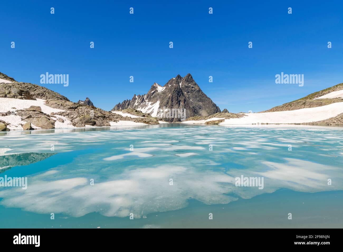 Thawing mountain lake with ice floes in summer under a blue sky near St. Anton am Arlberg. Patteriol in the background. Verwall, Tyrol, Austria Stock Photo