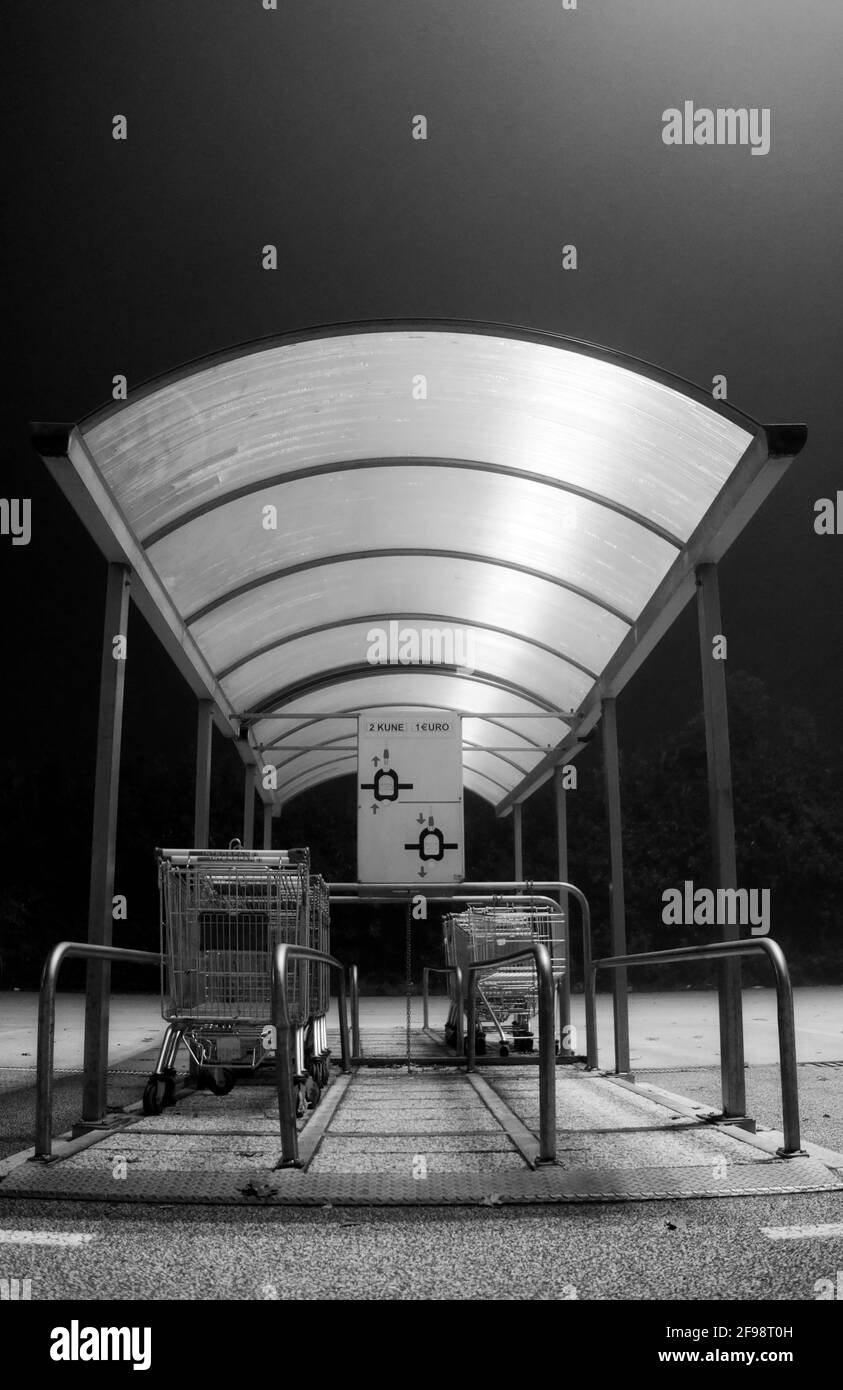 Vertical grayscale shot of a shopping cart station on a quiet night