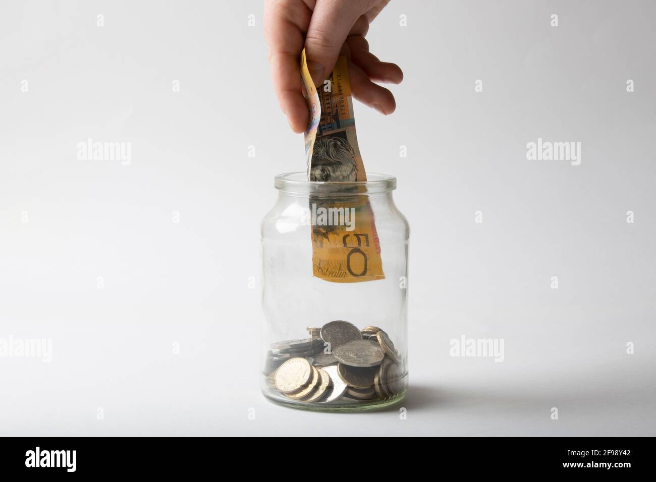 Hand holding Australian 50 dollar note over coin jar. Stock Photo