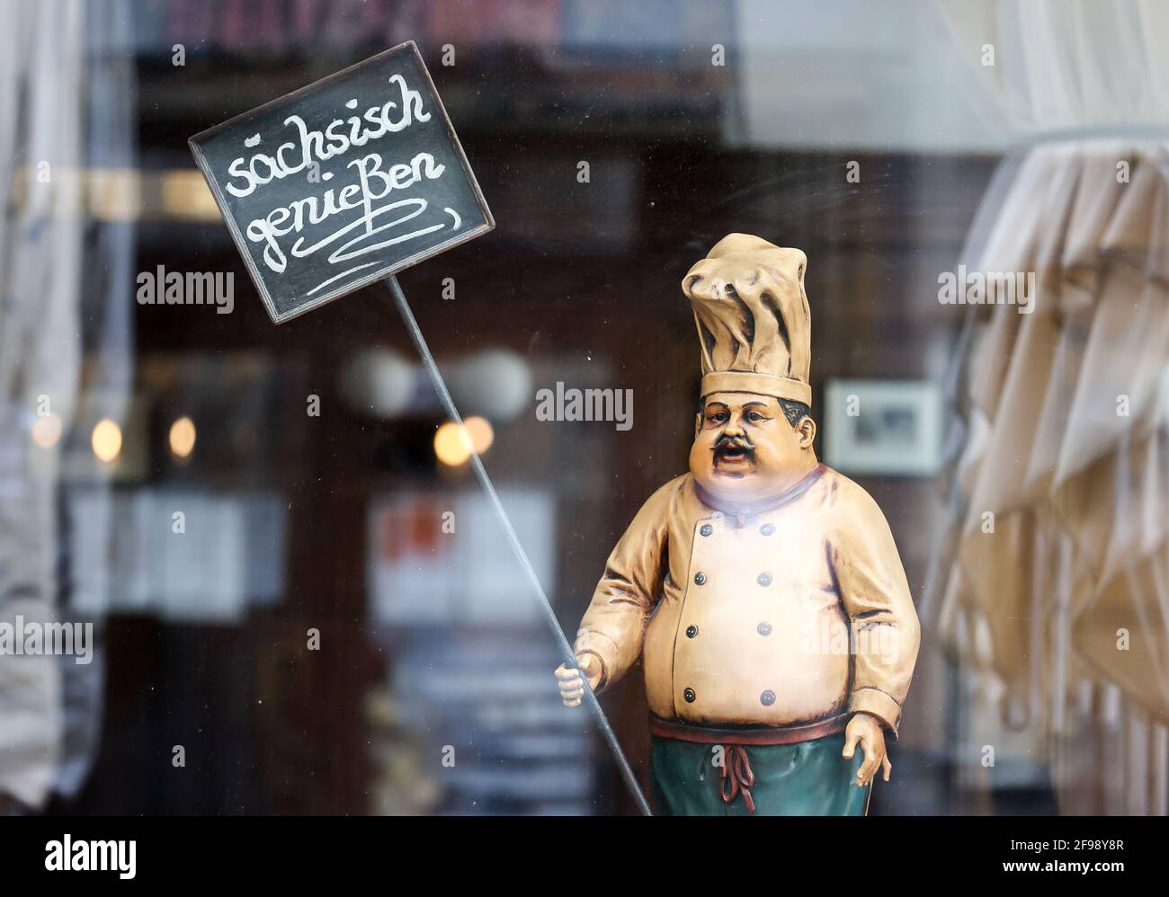 Leipzig, Germany. 15th Apr, 2021. The figure of a cook holds a sign 'sächsisch genießen' (enjoy Saxony) in the window of a restaurant closed due to corona. Credit: Jan Woitas/dpa-Zentralbild/ZB/dpa/Alamy Live News Stock Photo