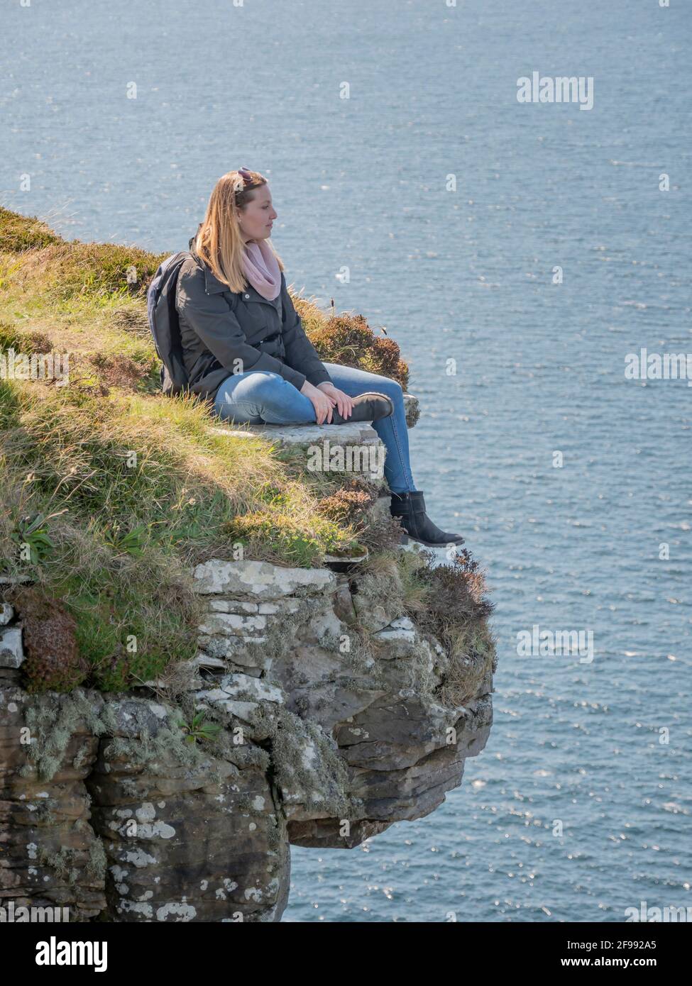 Young woman sitting on the edge of a cliff at the Irish west coast
