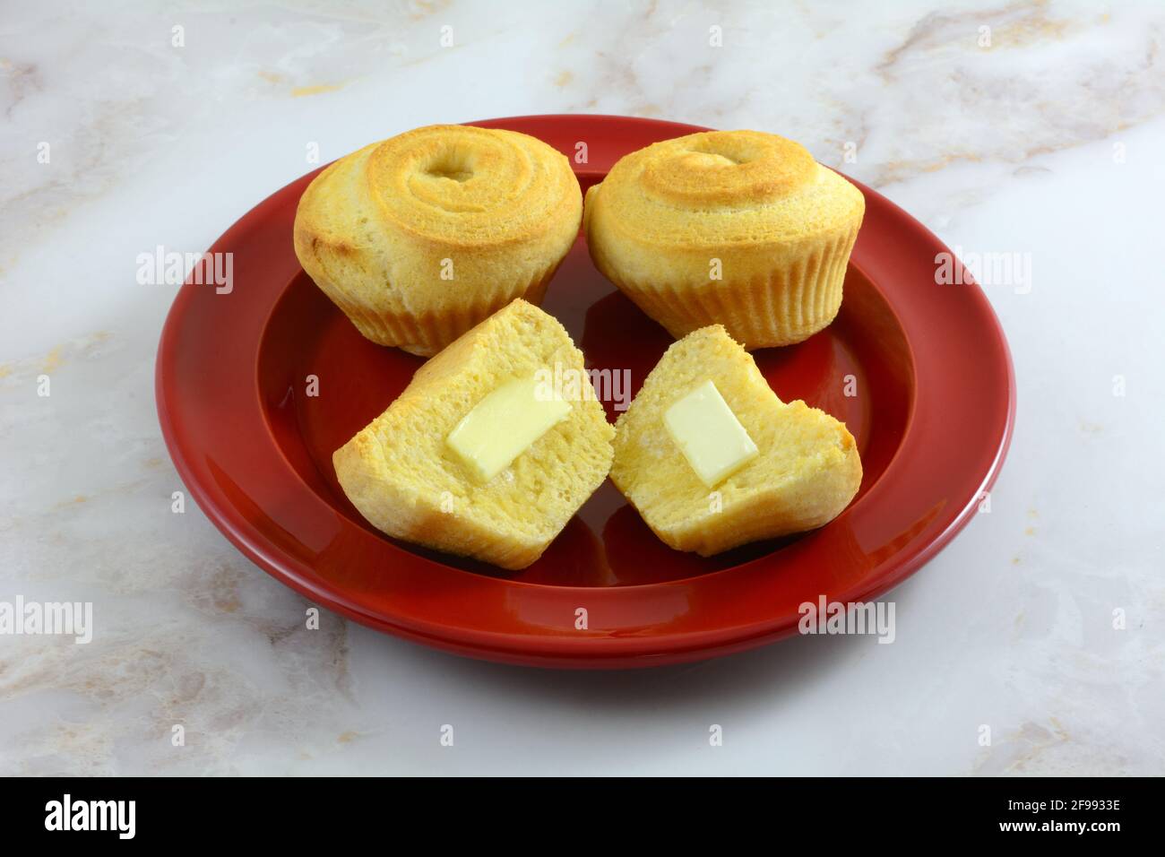 Corn swirl muffins with butter pats on halves on red bread plate Stock Photo