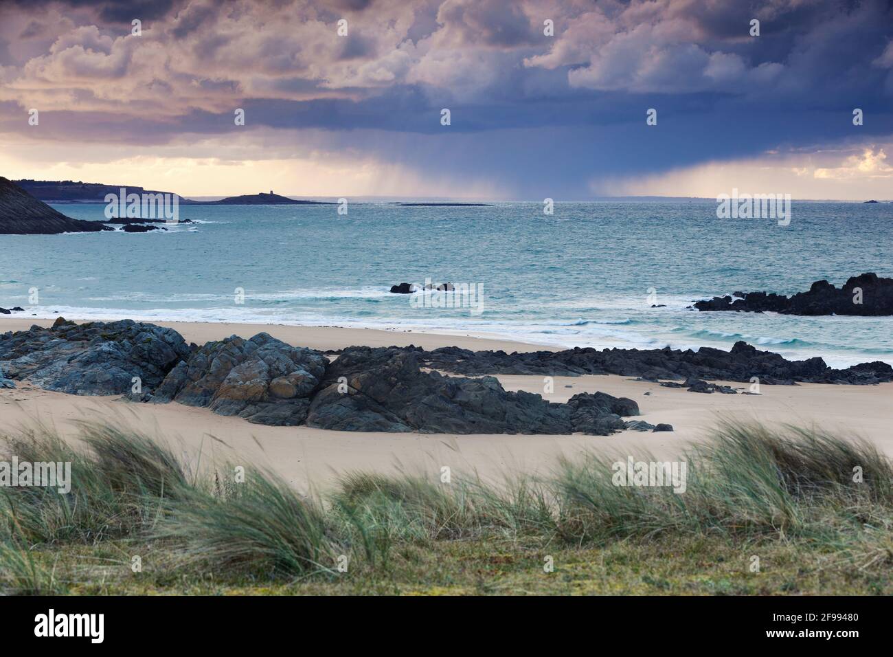 A storm is moving in the distance across the sea at Pleherel Plage, between Cap Frehel and the tidal island Ilot Michel. Brittany, France Stock Photo