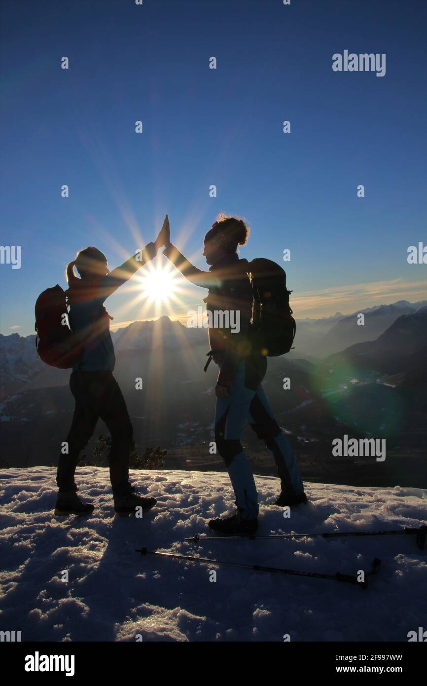 Winter hike to the Signalkopf (1895 meters) sunset with a view of the Wetterstein Mountains, 2 young women clap, clap, Europe, Germany, Bavaria, Upper Bavaria, Isar Valley, Krün Stock Photo