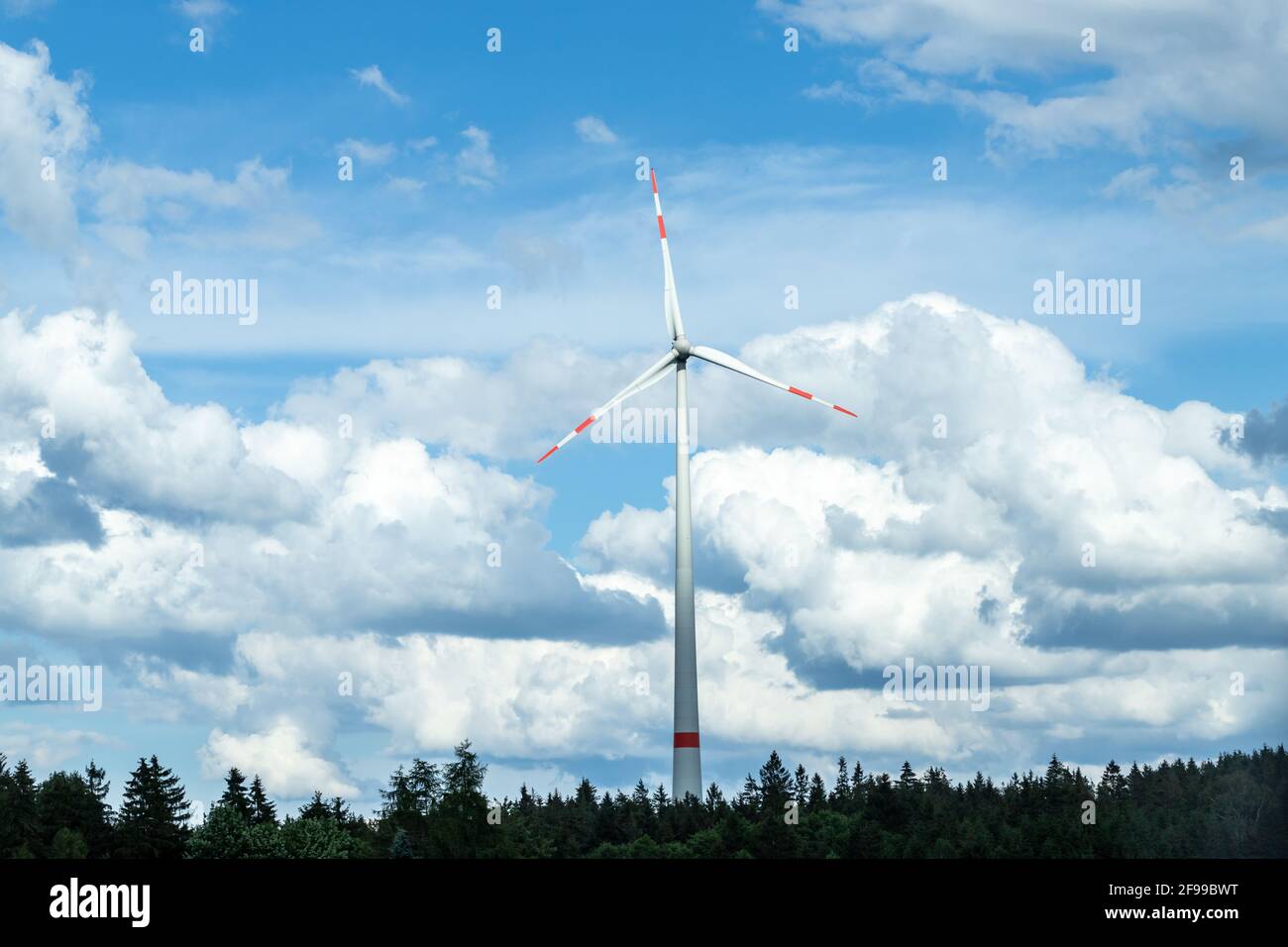 A pinwheel above a forest against a blue sky with clouds. Stock Photo