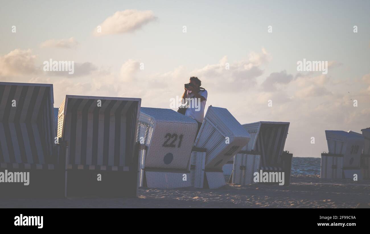 Paparazzi - a photographer stands on a beach chair and photographs a scene at sunset by the sea. Stock Photo