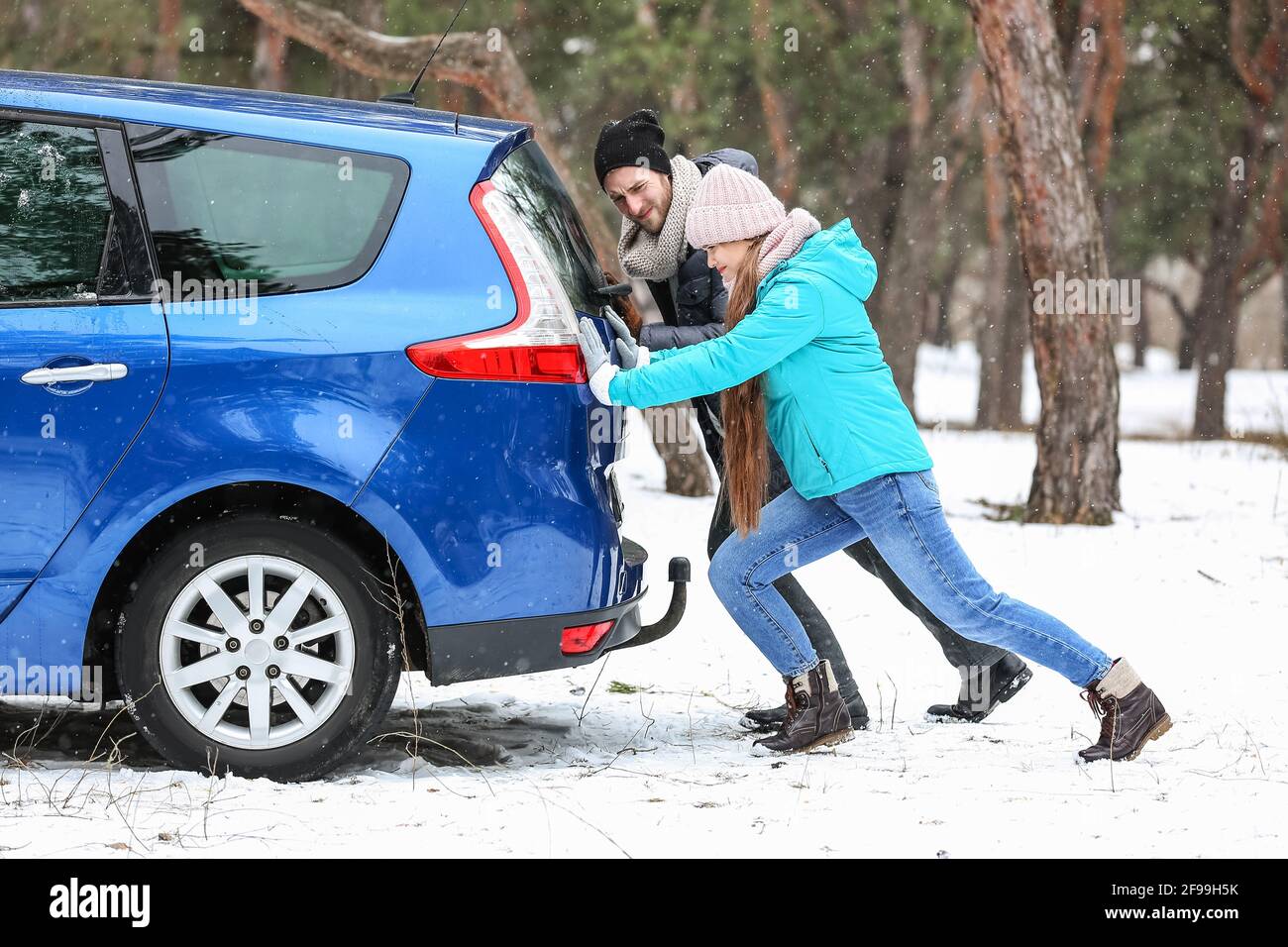 Couple pushing broken car on winter day Stock Photo