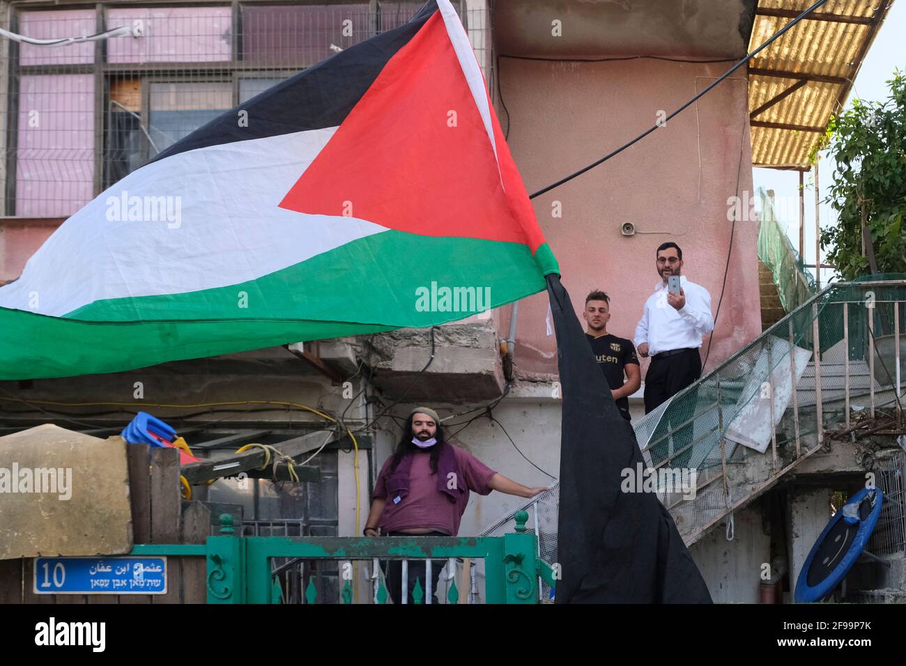 Palestinians and Israeli left-wing activists hold up the Palestinian flag in front of a house which was occupied by Jewish settlers during a demonstration against settlement activity in Sheikh Jarrah a predominantly Palestinian neighborhood on April 16, 2021, in East Jerusalem, Israel. The Palestinian neighborhood of Sheikh Jarrah is currently the center of a number of property disputes between Palestinians and Israelis. Some houses were occupied by Israeli settlers following a court ruling. Stock Photo