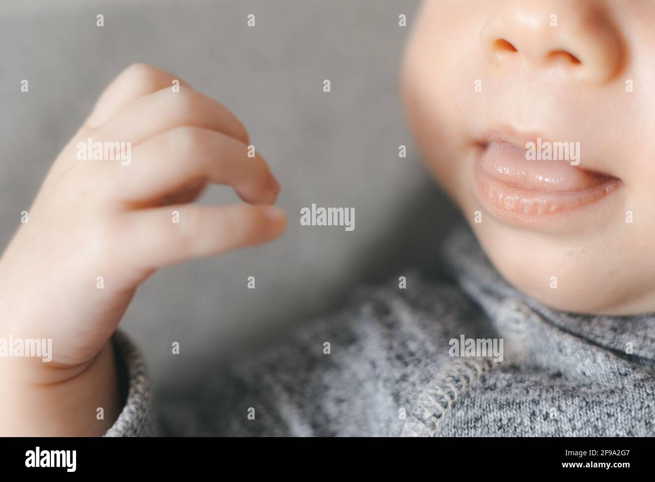 Cropped photo of newborn baby sleeping on gray background, open mouth