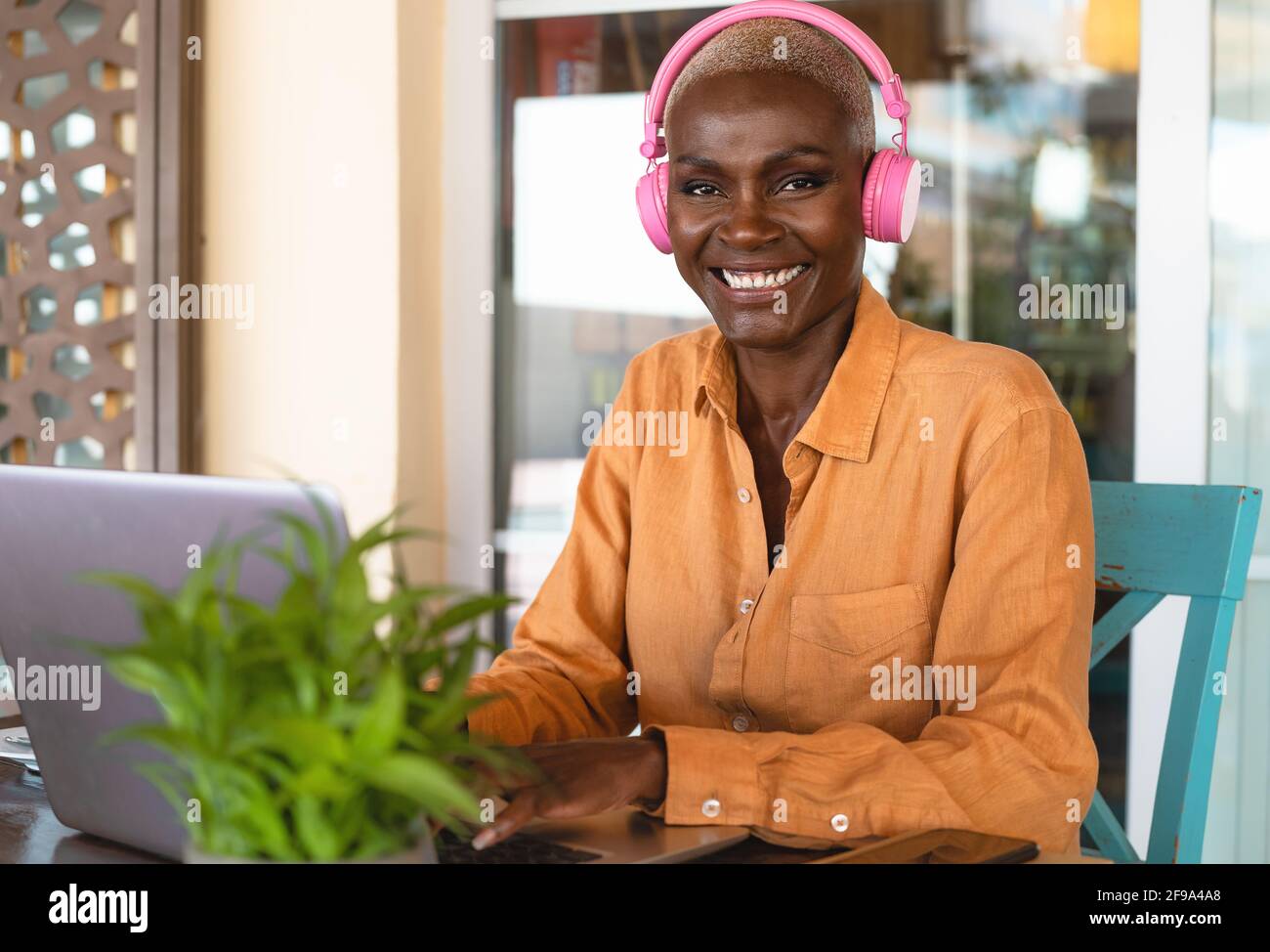 Smiling African woman using laptop and listening music with headphones in bar restaurant - Digital nomad and freelance lifestyle concept Stock Photo