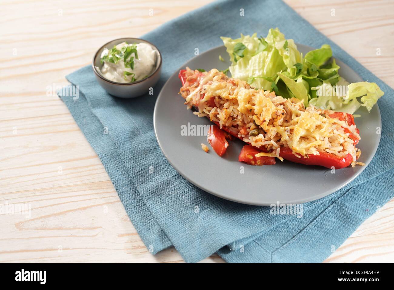 Baked pointed bell pepper stuffed with rice, tuna, tomatoes and cheese on a blue plate with lettuce salad, dip and parsley garnish, napkin and bright Stock Photo