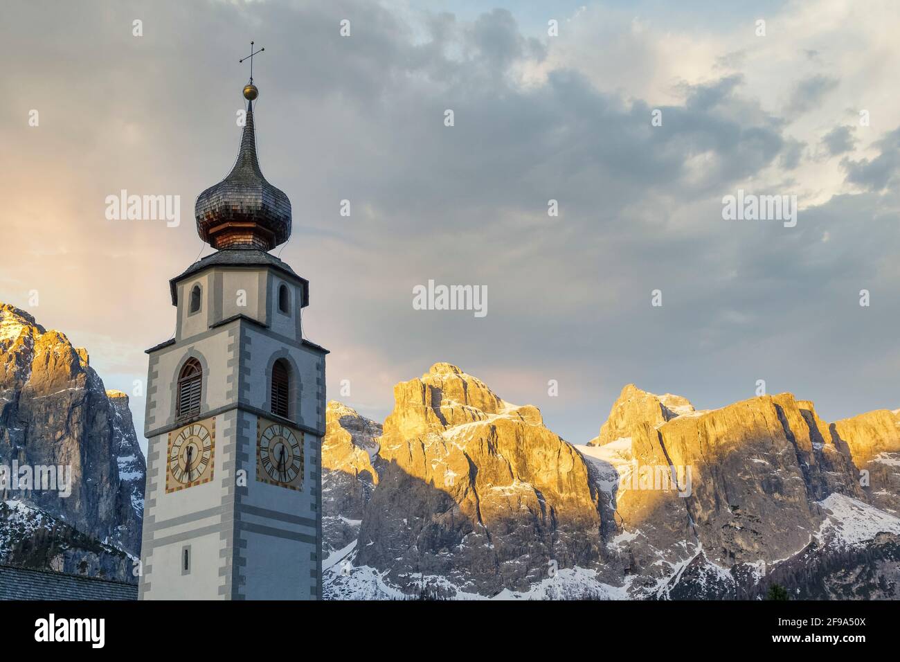 Colfosco, Alta Badia, Dolomites, South Tyrol, Italy. The bell tower of the San Vigilio church with the Sella group in background Stock Photo