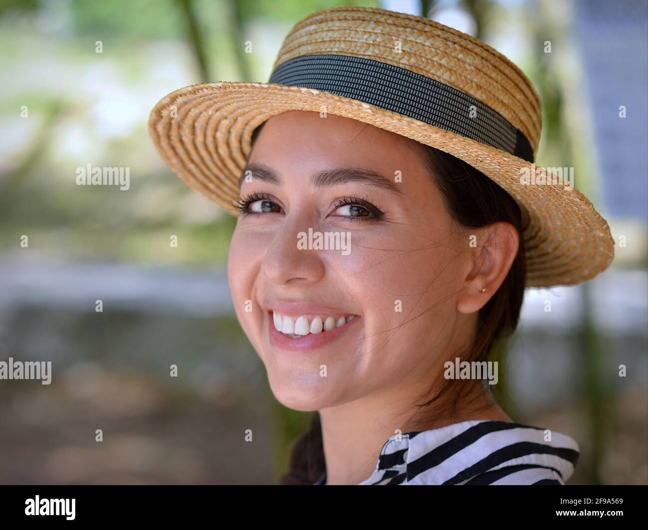 Attractive cheerful young Mexican eco farm woman and wears a classical Panama straw hat and smiles with her beautiful long eyelashes for the camera. Stock Photo