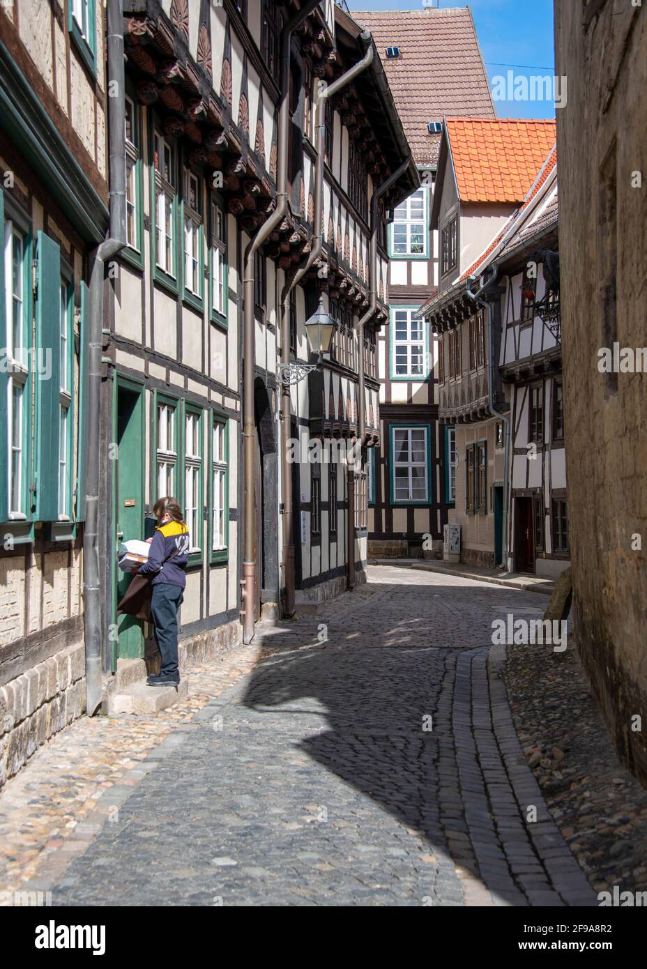 Germany, Saxony-Anhalt, Quedlinburg, narrow alley with half-timbered houses, postal worker carries letters from, World Heritage City of Quedlinburg. Stock Photo