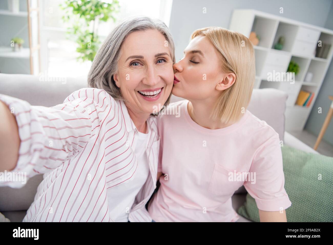 Photo of happy cheerful mom and daughter take selfie smile kiss cheek parent indoors inside