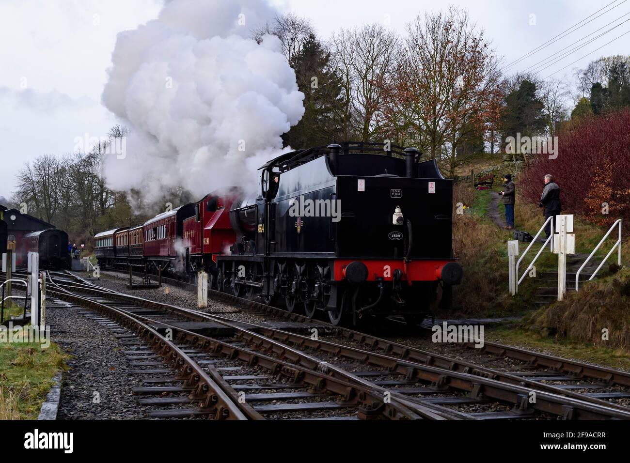 Historic steam trains or locos puffing smoke clouds (engine driver in cab, enthusiasts & cameras) - Oxenhope Station sidings, Yorkshire, England, UK. Stock Photo