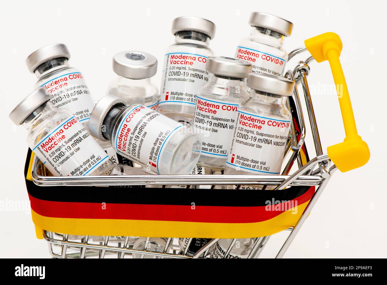 Original COVID-19 vaccination ampoule from Moderna and Pfizer-BioNTech symbolically in a shopping trolley with a German-colored banderole Stock Photo