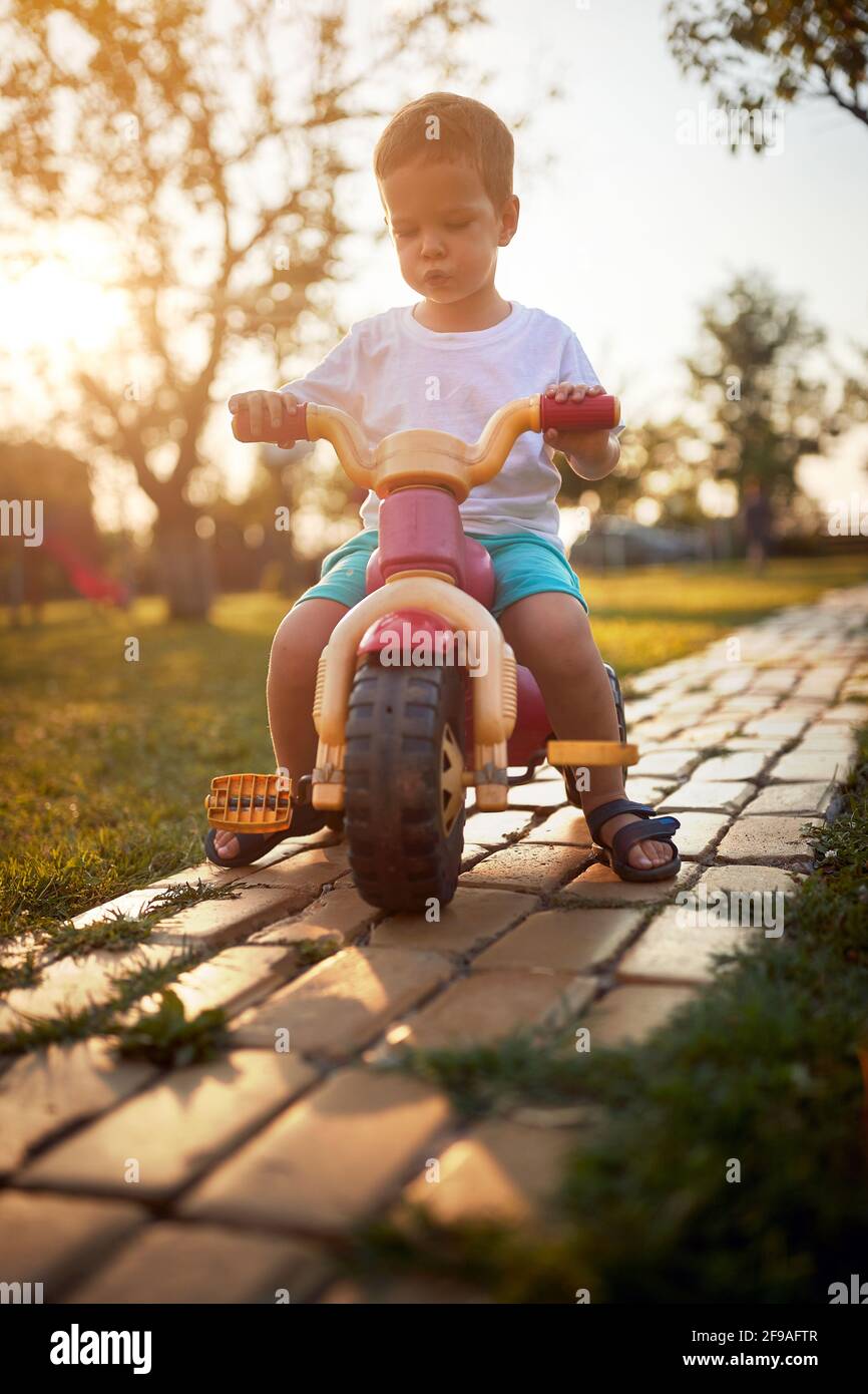 A little boy enjoying riding a bike in the yard in the farm on a beautiful sunny day. Farm, countryside, summer Stock Photo