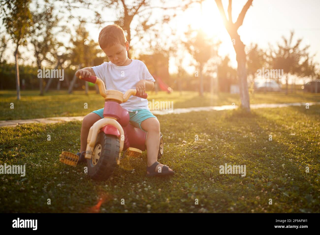A little boy riding a bike in the yard in the farm on a beautiful sunny day. Farm, countryside, summer Stock Photo