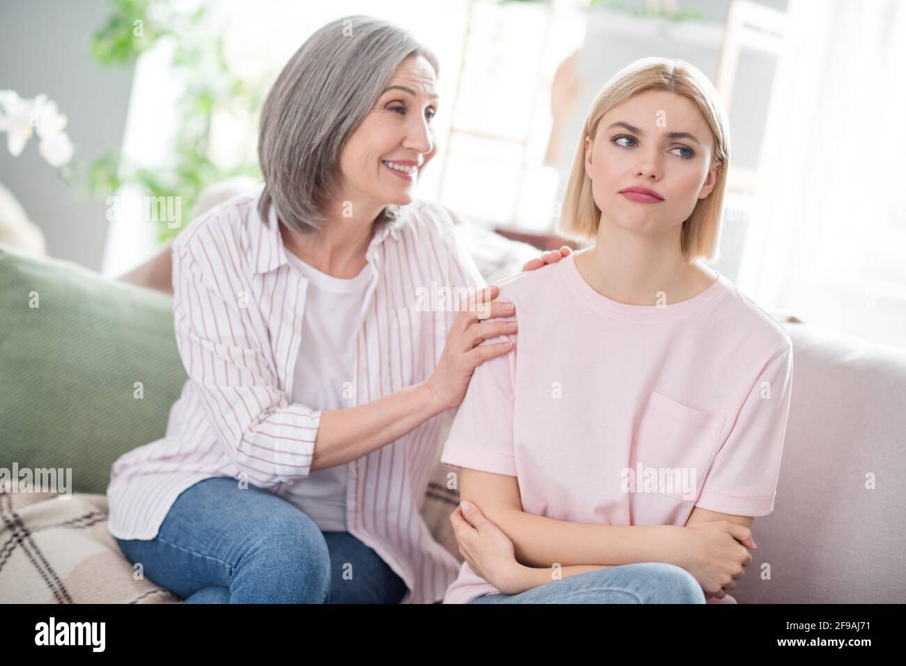 Photo of unhappy sad young woman and happy cheerful grandmother say sorry mistake indoors inside house home Stock Photo