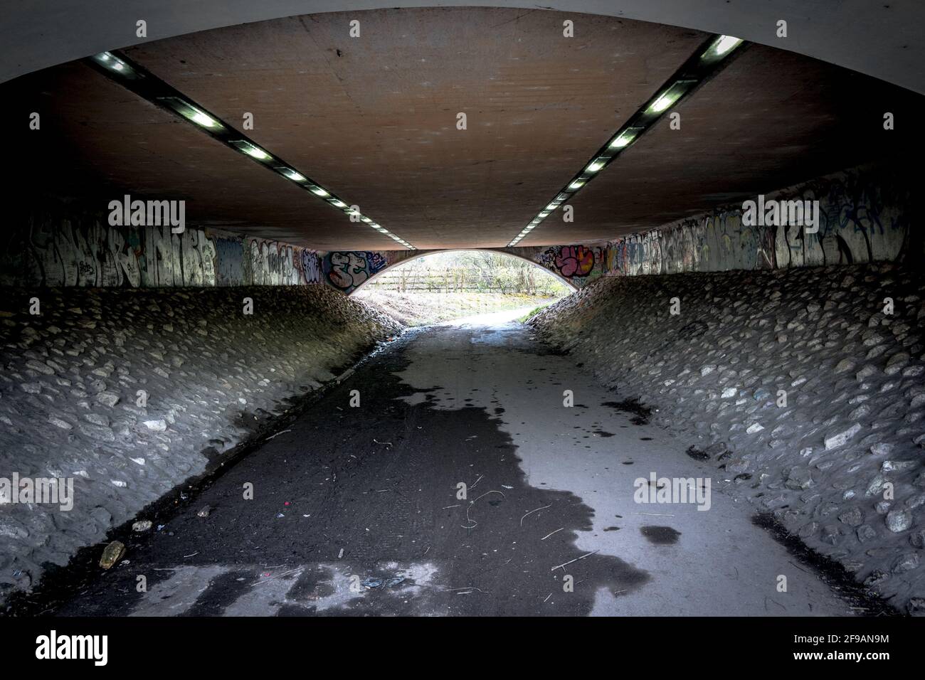 Strip lighting illuminating a predestian underpass with graffiti. Stock Photo