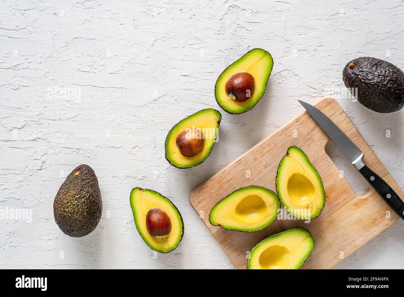 Top view of fresh halved avocados on a white surface, with a cutting ...