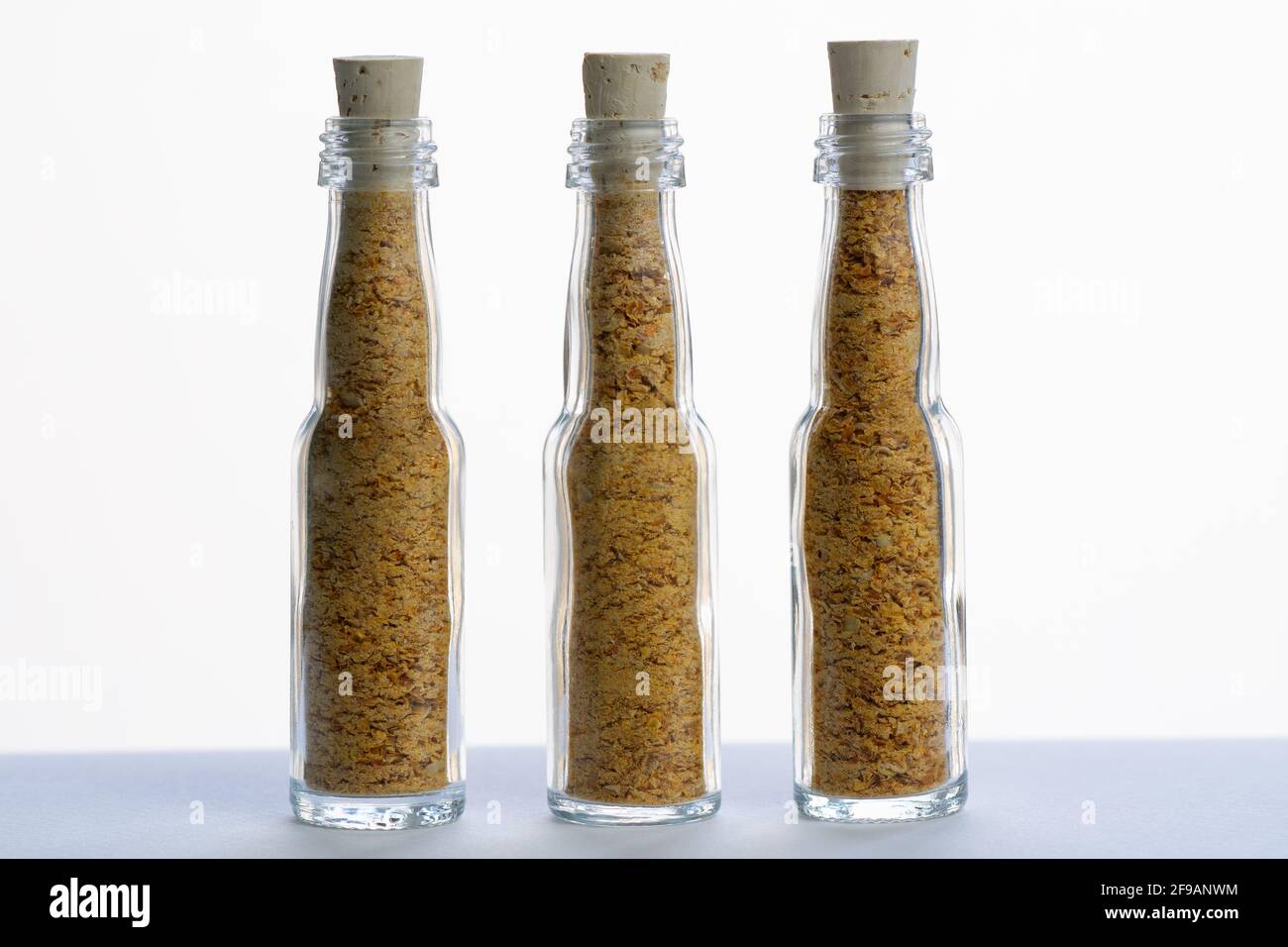 Ground dry Trinidad Scorpion Yellow peppers in three small glass bottles. Flacons are sealed with cork stoppers. Stock Photo