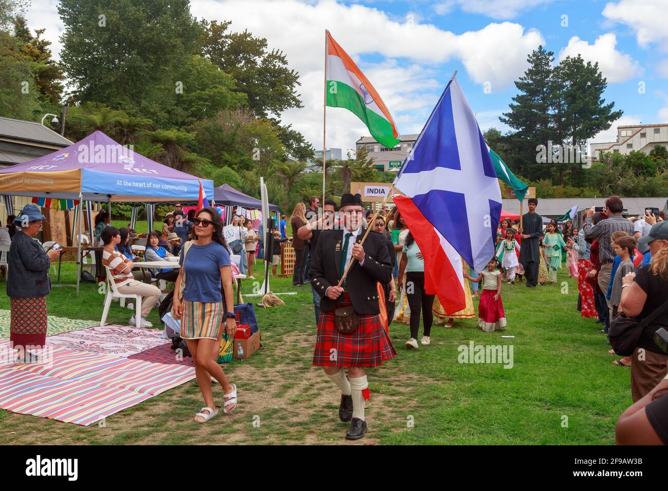 A Scottish man wearing a kilt and holding the flag of Scotland leading a multicultural parade. Tauranga, New Zealand Stock Photo