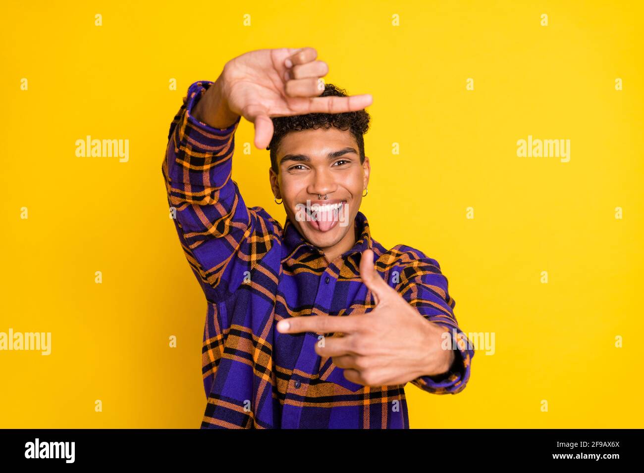 Photo of young cheerful afro man happy smile grimace tongue-out make fingers frame snapshot isolated over yellow color background Stock Photo