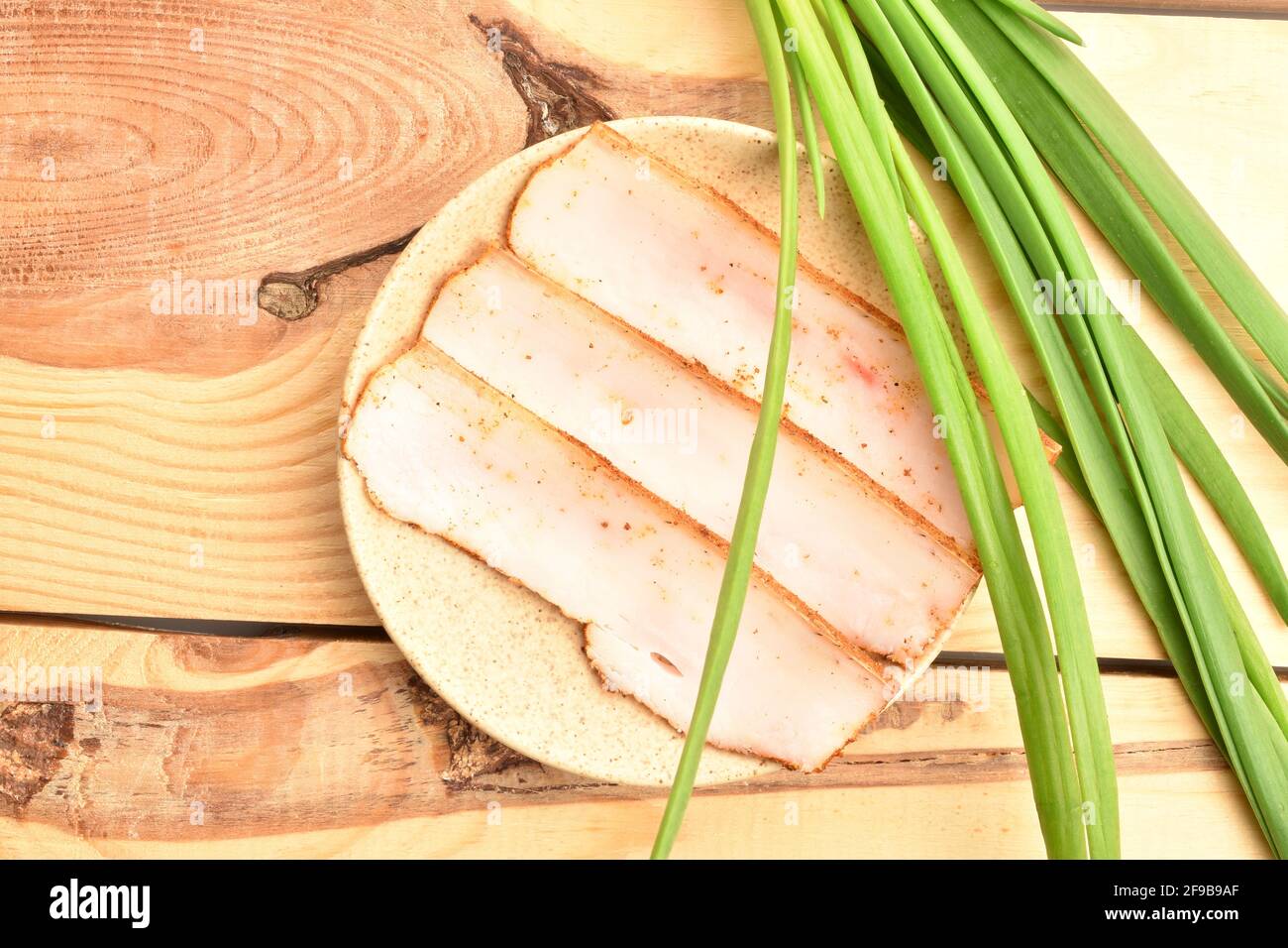 Three slices of delicious, calorie, tasty, piquant bacon with bread and fresh onions on a ceramic saucer, standing on a wooden table. Stock Photo