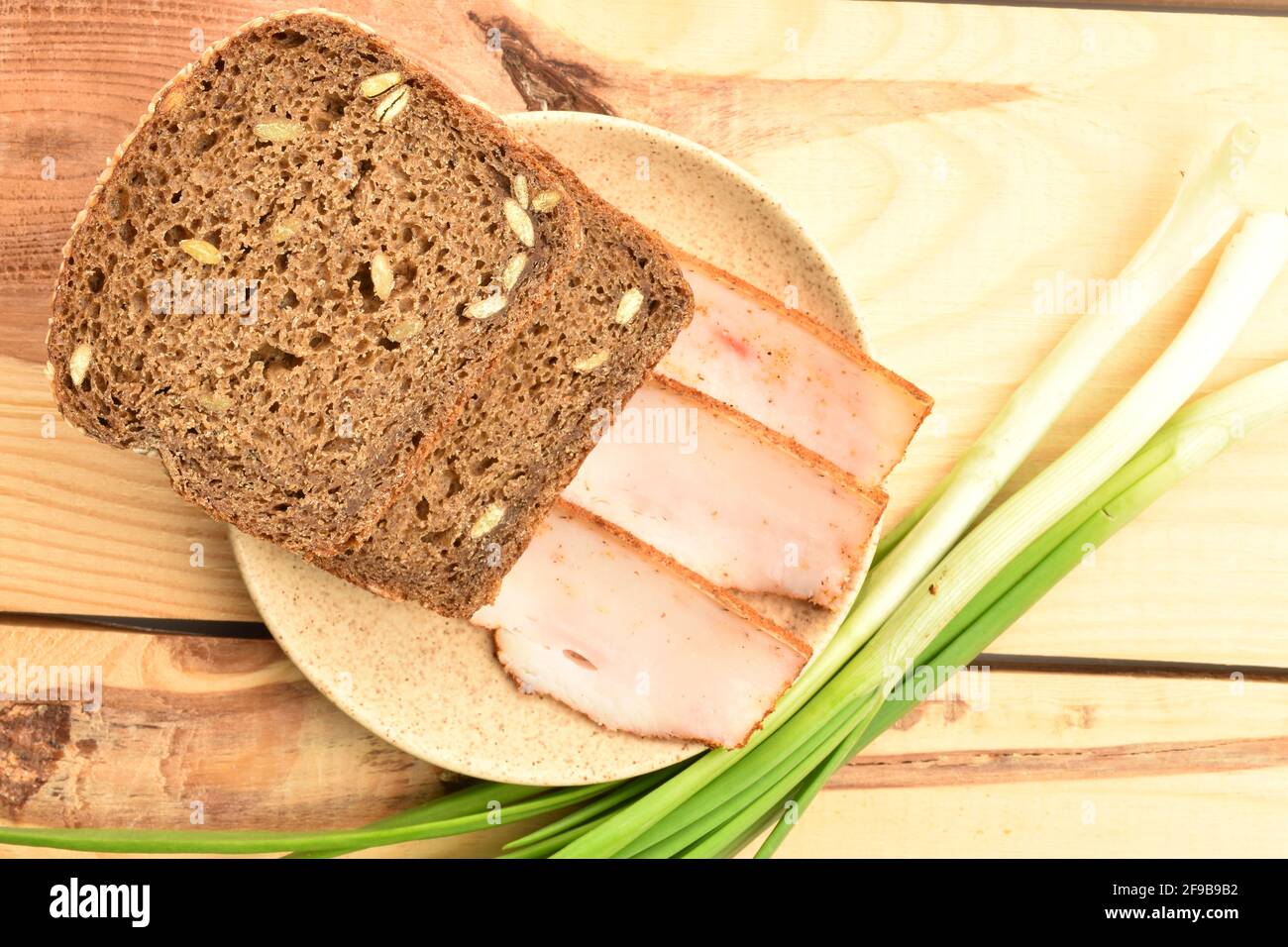 Three slices of delicious, calorie, tasty, piquant bacon with bread and fresh onions on a ceramic saucer, standing on a wooden table. Stock Photo