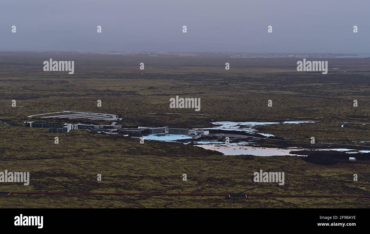 Aerial view of Blue Lagoon spa resort with pools of blue colored thermal water located between volcanic lava fields with town Keflavik in background. Stock Photo