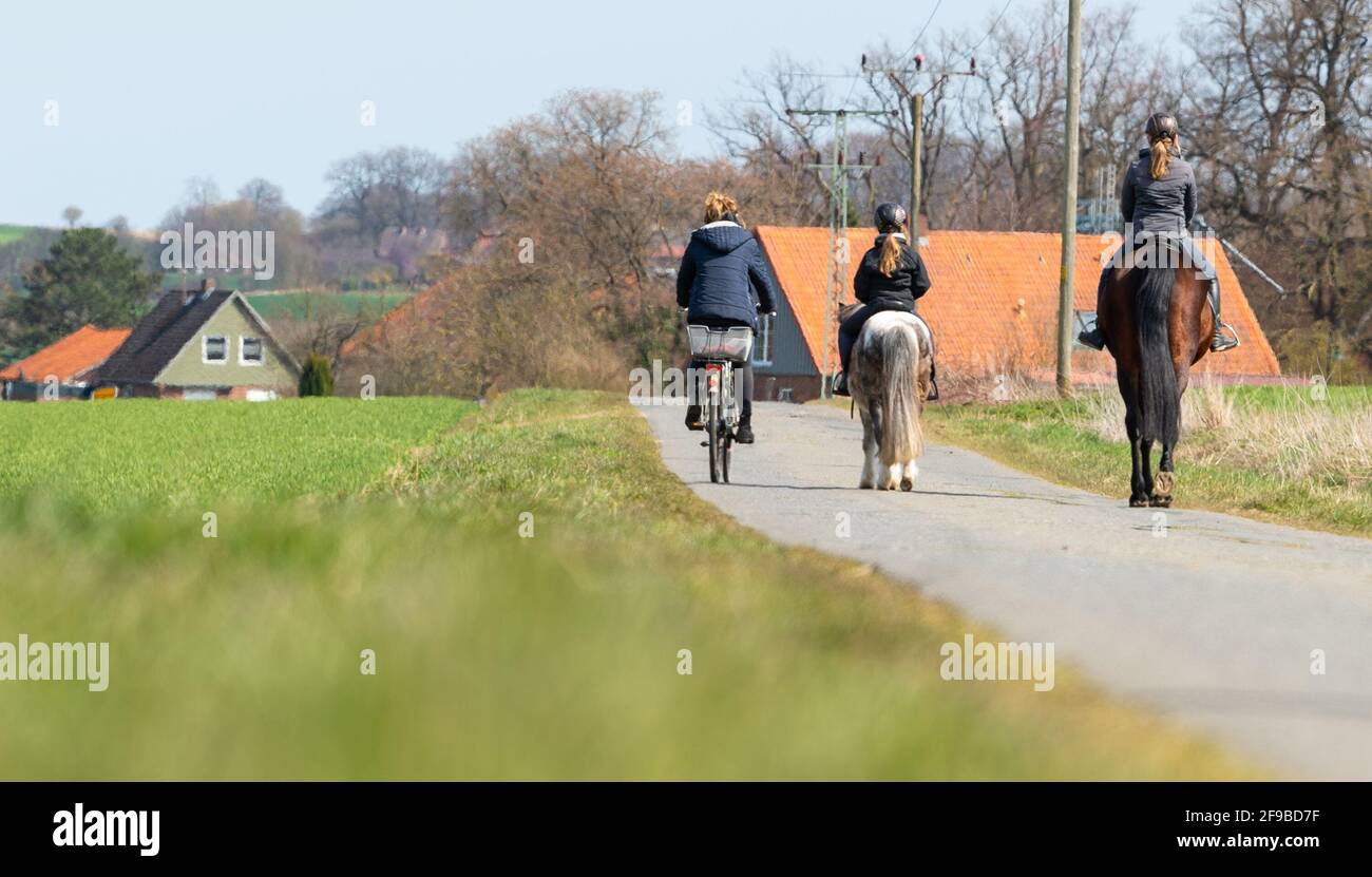 Wessenstedt, Germany. 17th Apr, 2021. Two girls are riding their horses and one on a bicycle between fields and meadows. Credit: Philipp Schulze/dpa/Alamy Live News Stock Photo