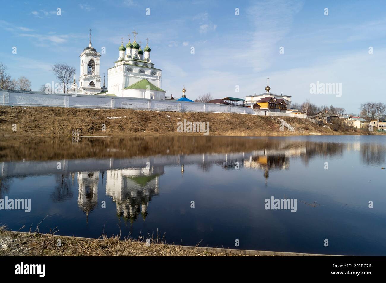 Christian church on the river bank against the background of a blue sky with a white cloud. Beautiful landscape in spring time Stock Photo