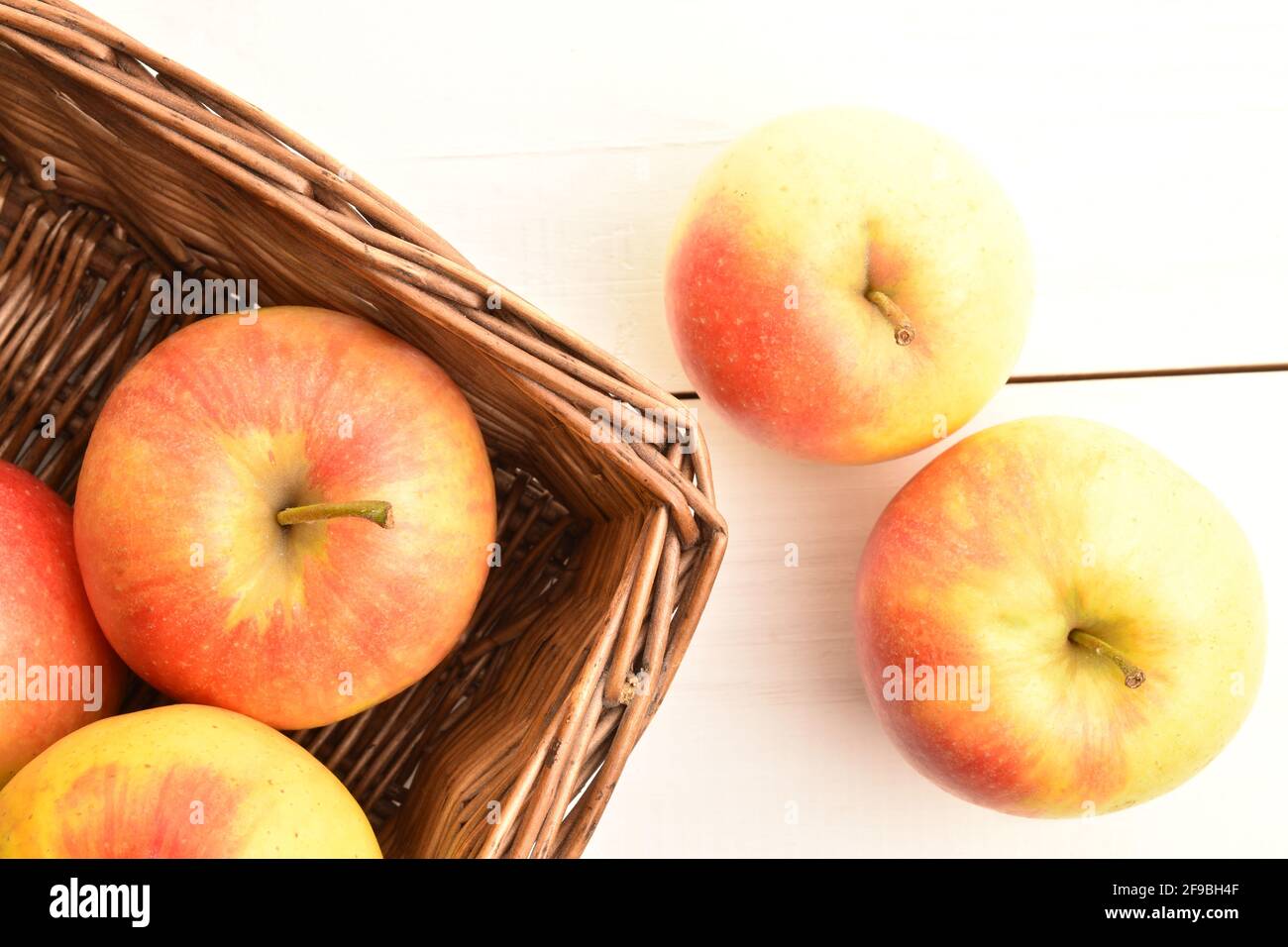 Several ripe organic, juicy, aromatic apples in a wicker basket of vines, close-up, on a painted wooden table. Stock Photo
