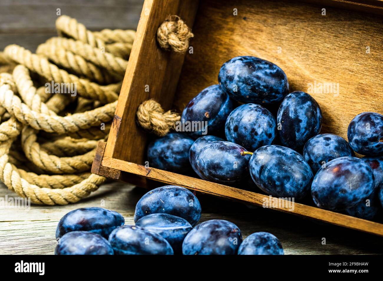 Close-up shot of ripe blue plums in a wooden crate in a rustic composition. Stock Photo