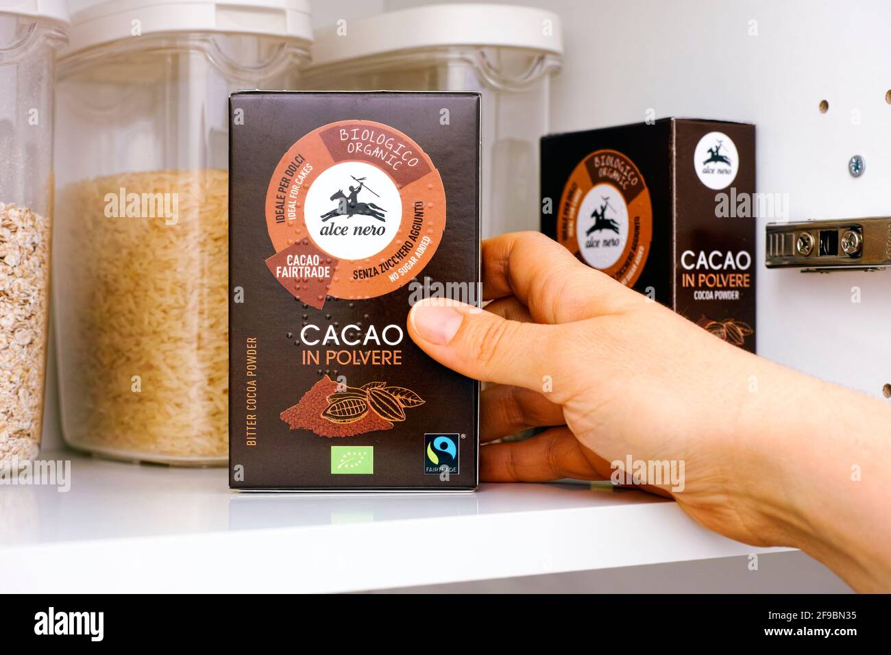 Tambov, Russian Federation - March 19, 2021 Woman hand taking Organic Bitter Cocoa Powder pack by Alce Nero out of a kitchen cupboard Stock Photo