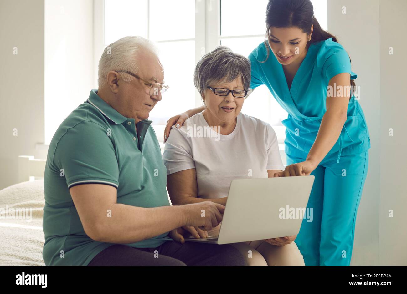 Nursing home worker teaching her happy senior patients to use modern laptop computer Stock Photo