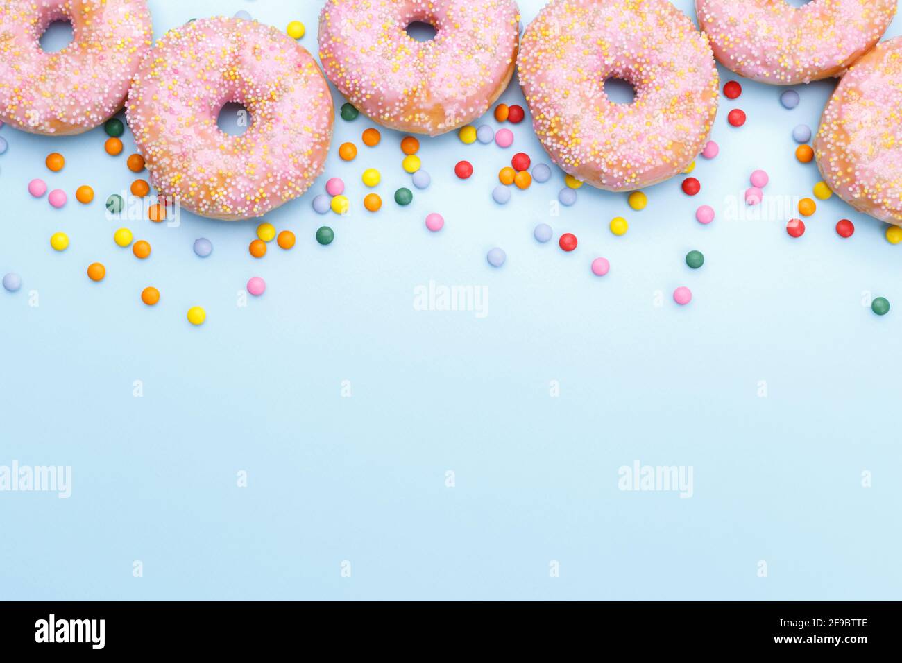 Pink doughnuts and candies on blue background, copy space flat lay Stock Photo