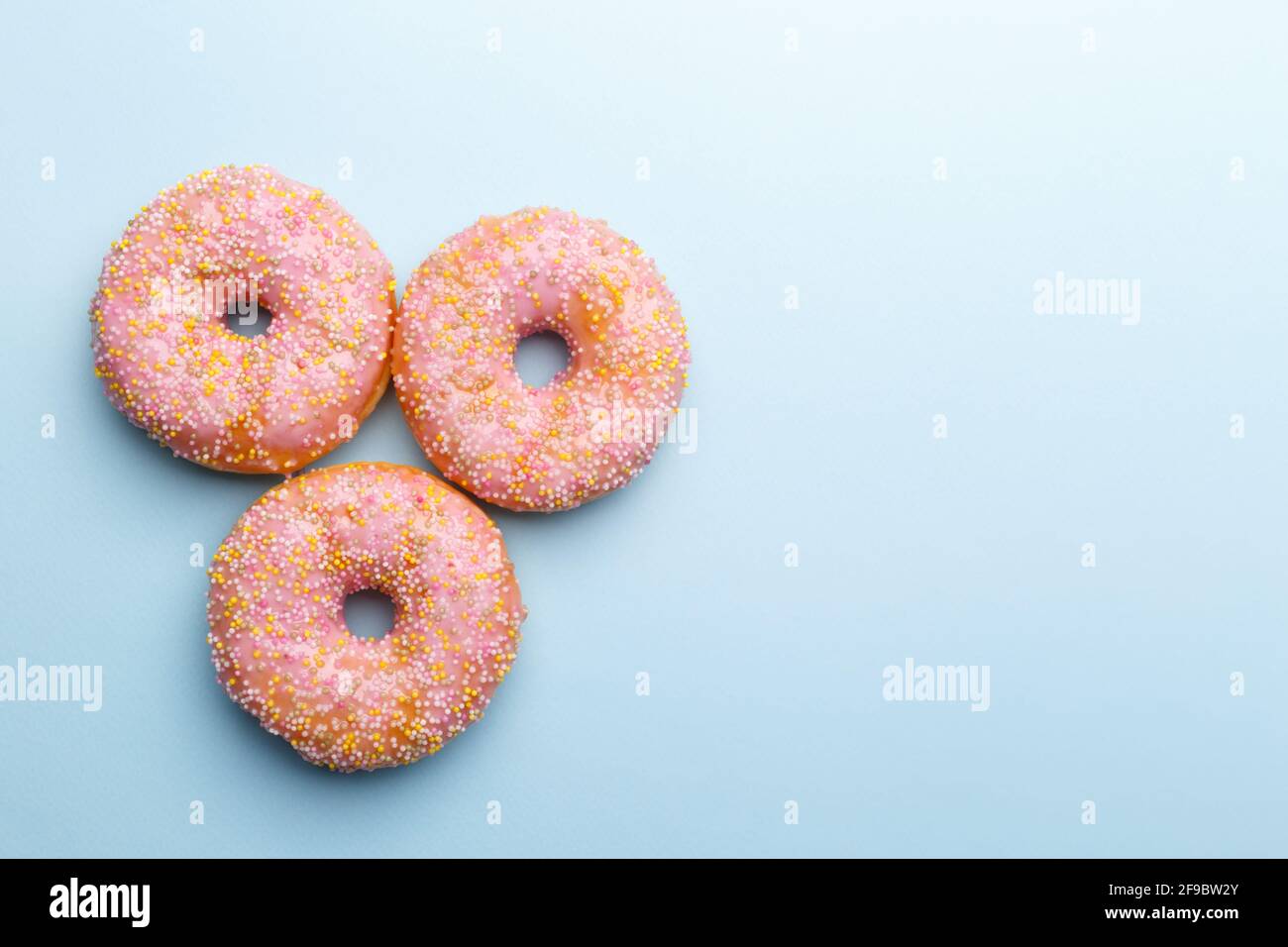 Pink doughnuts and candies on blue background, copy space flat lay Stock Photo