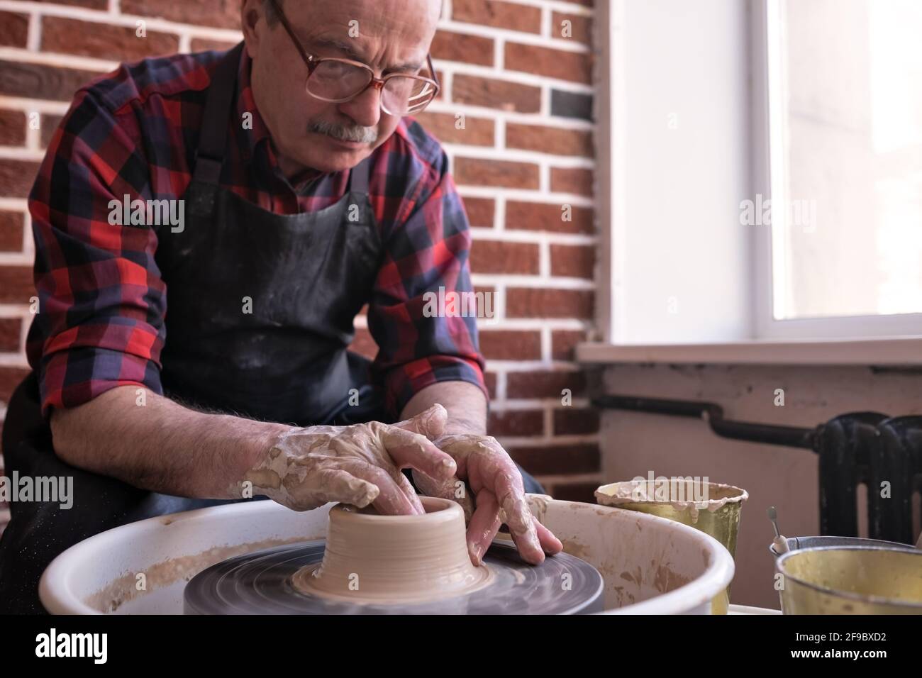Senior male potter creating bowl in pottery workshop. Hobby at old age ...