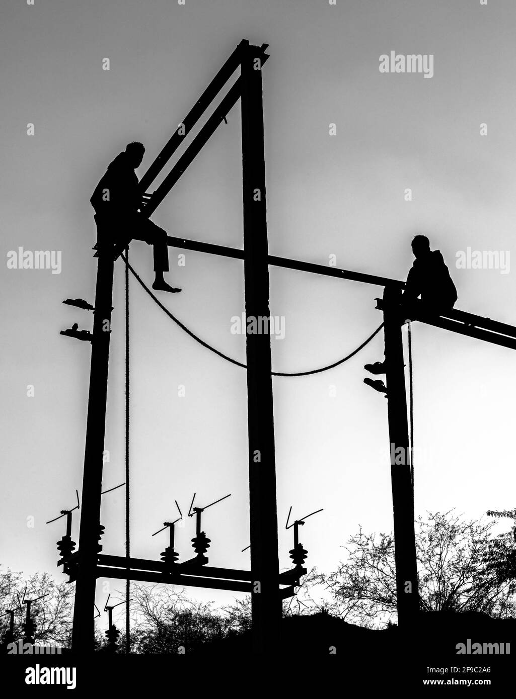 black and white silhouette of a two man sitting on electric pole. Stock Photo