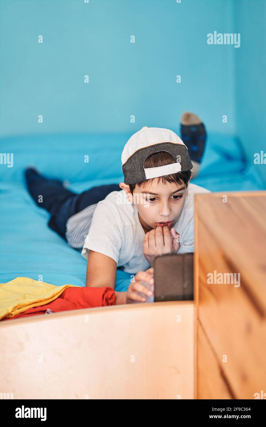 Boy lying on bed looking at tablet in room at home Stock Photo - Alamy