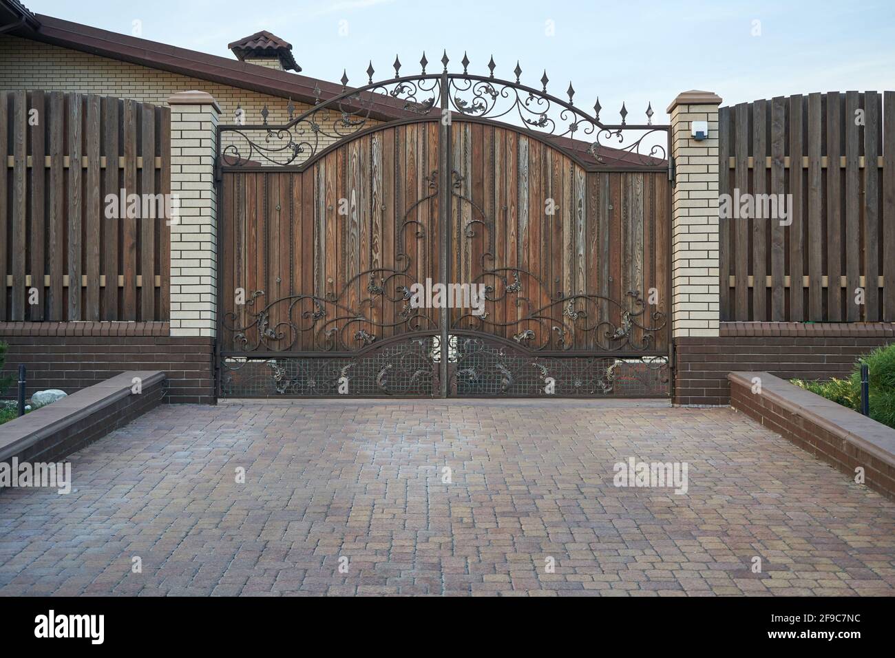 Metal wrought brown gates and wooden fence Stock Photo