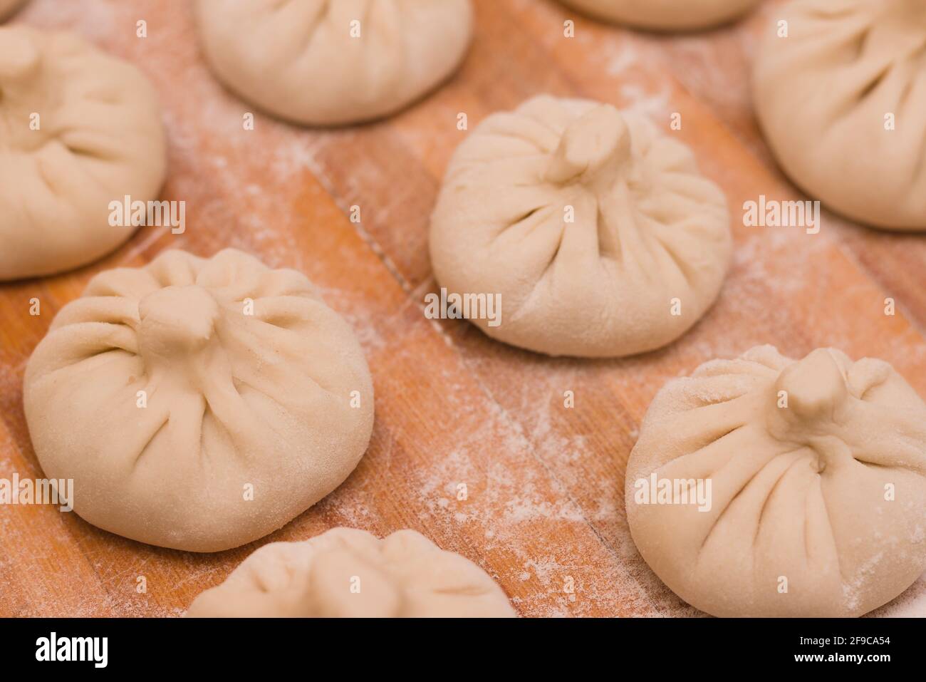 Three rows of homemade raw khinkali dumplings on a wooden board in flour Stock Photo